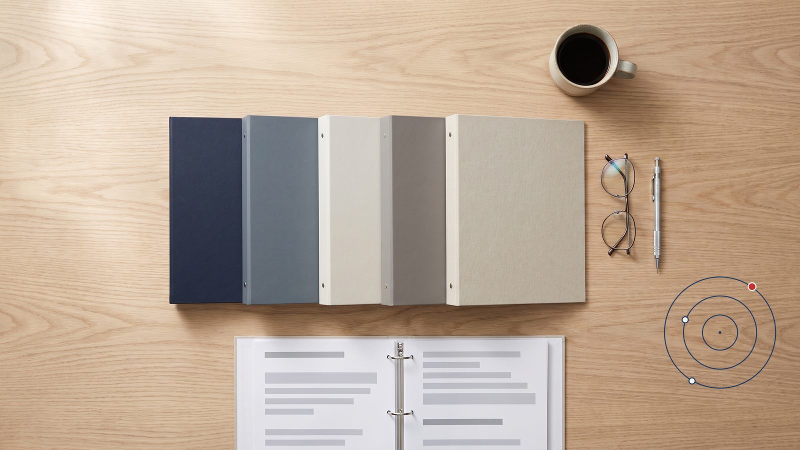 Five closed binders in graded shades of navy, gray and cream on a wood desk, beside an open report binder, reading glasses, a pen and a cup of coffee