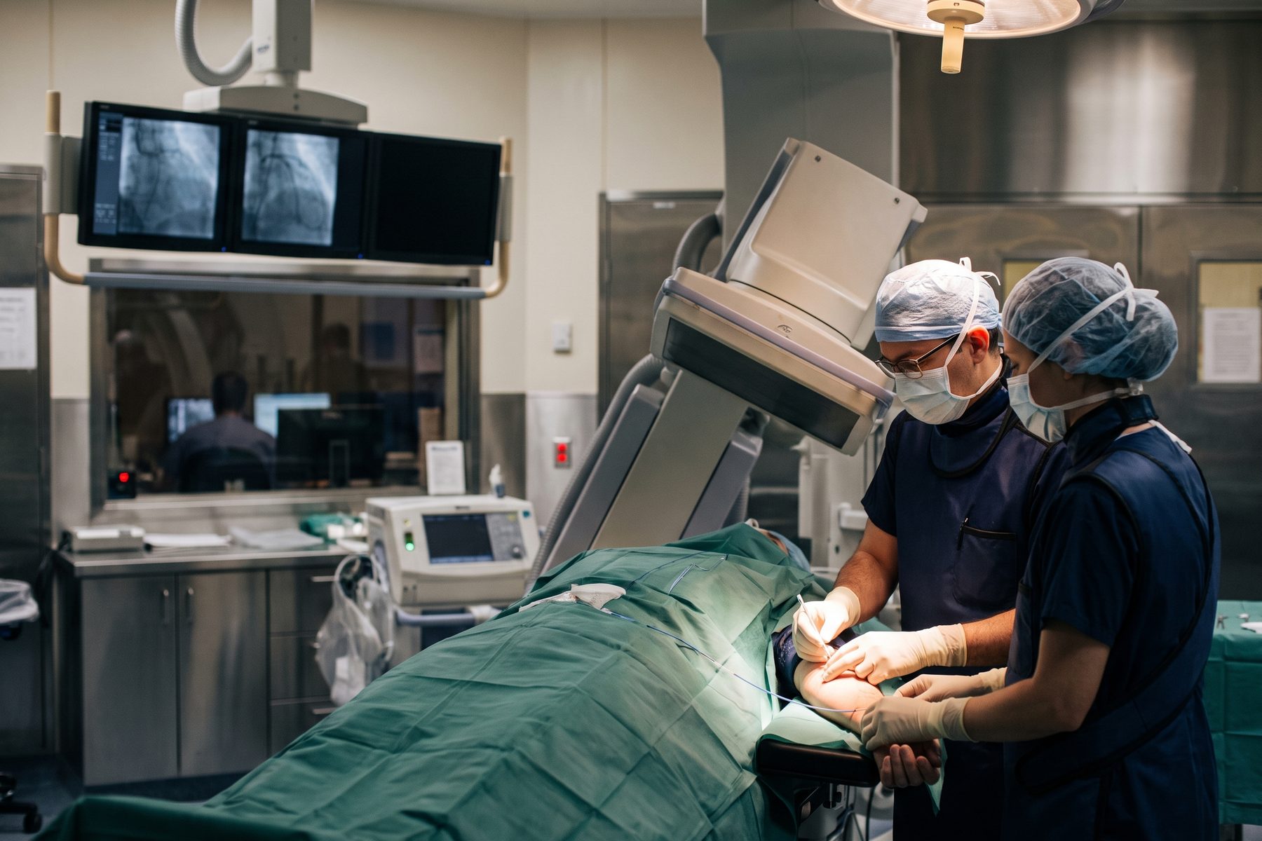 A cardiologist and scrub nurse guiding a catheter during a procedure in a cardiac catheterization laboratory.