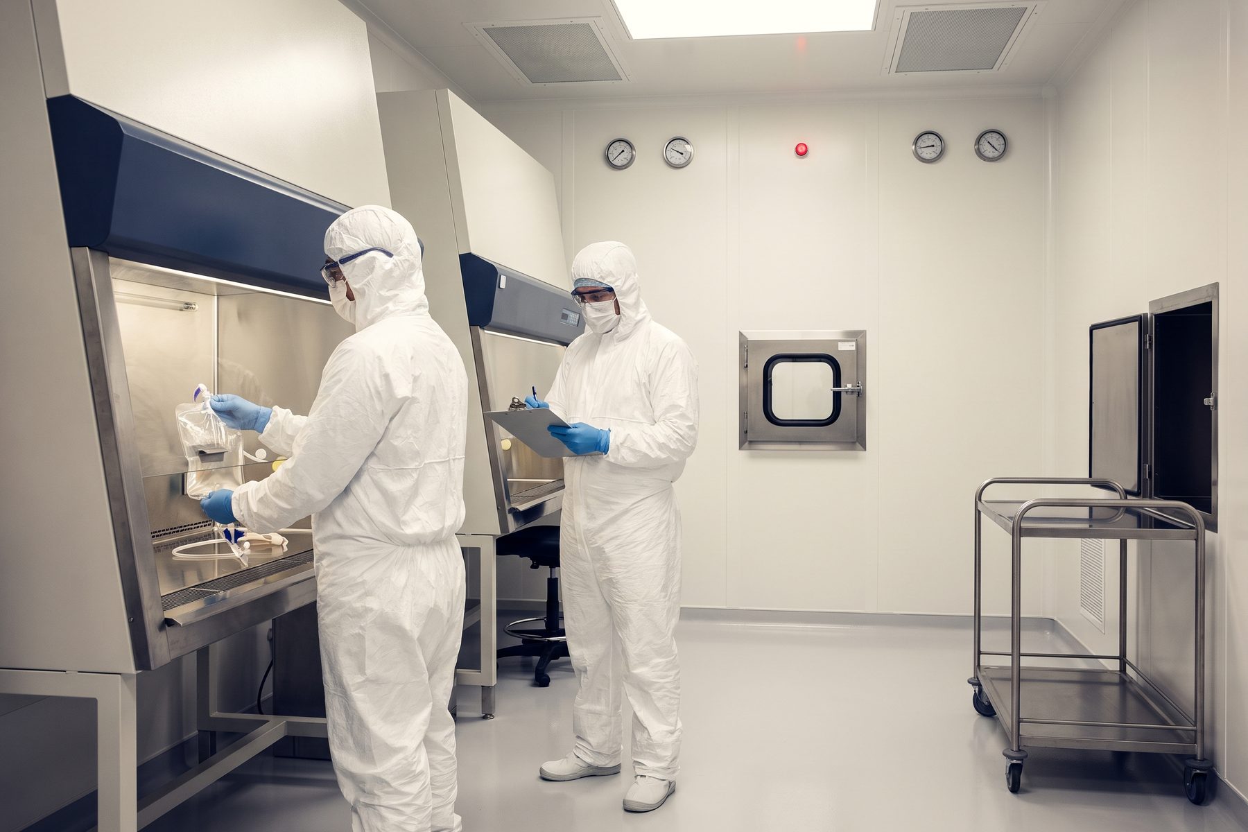 Two gowned technicians working at a biosafety cabinet in a GMP cleanroom.