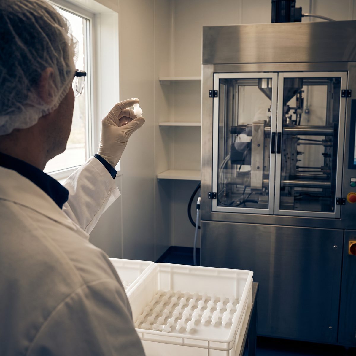 A supplier quality auditor inspecting a molded medical component beside an injection-molding press.