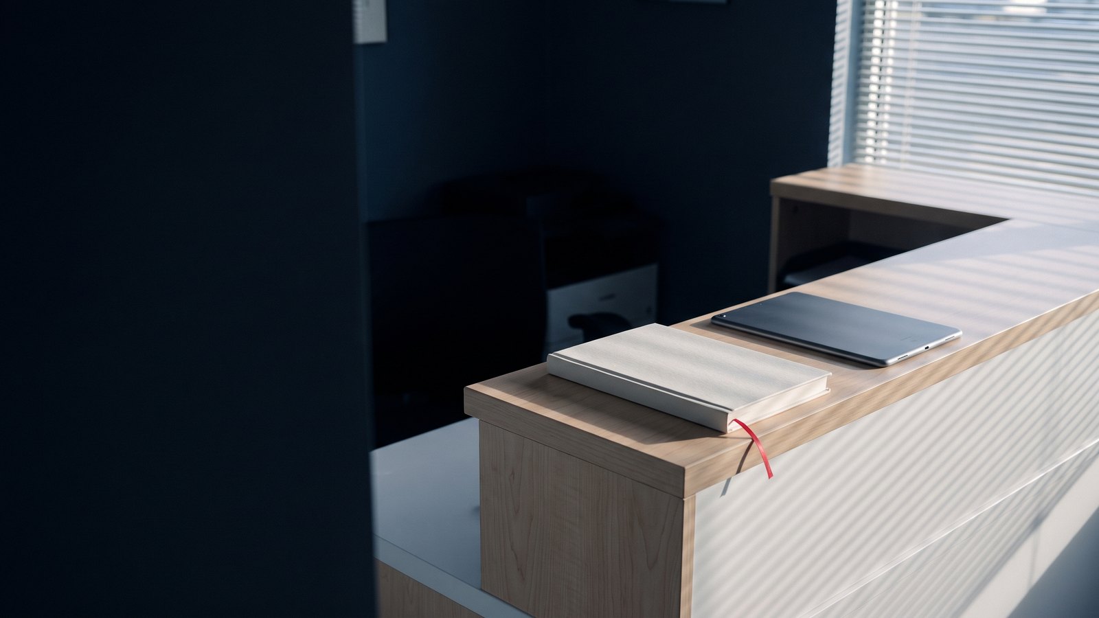 A tablet lying face down beside a closed appointment book on a clinic front desk at dawn