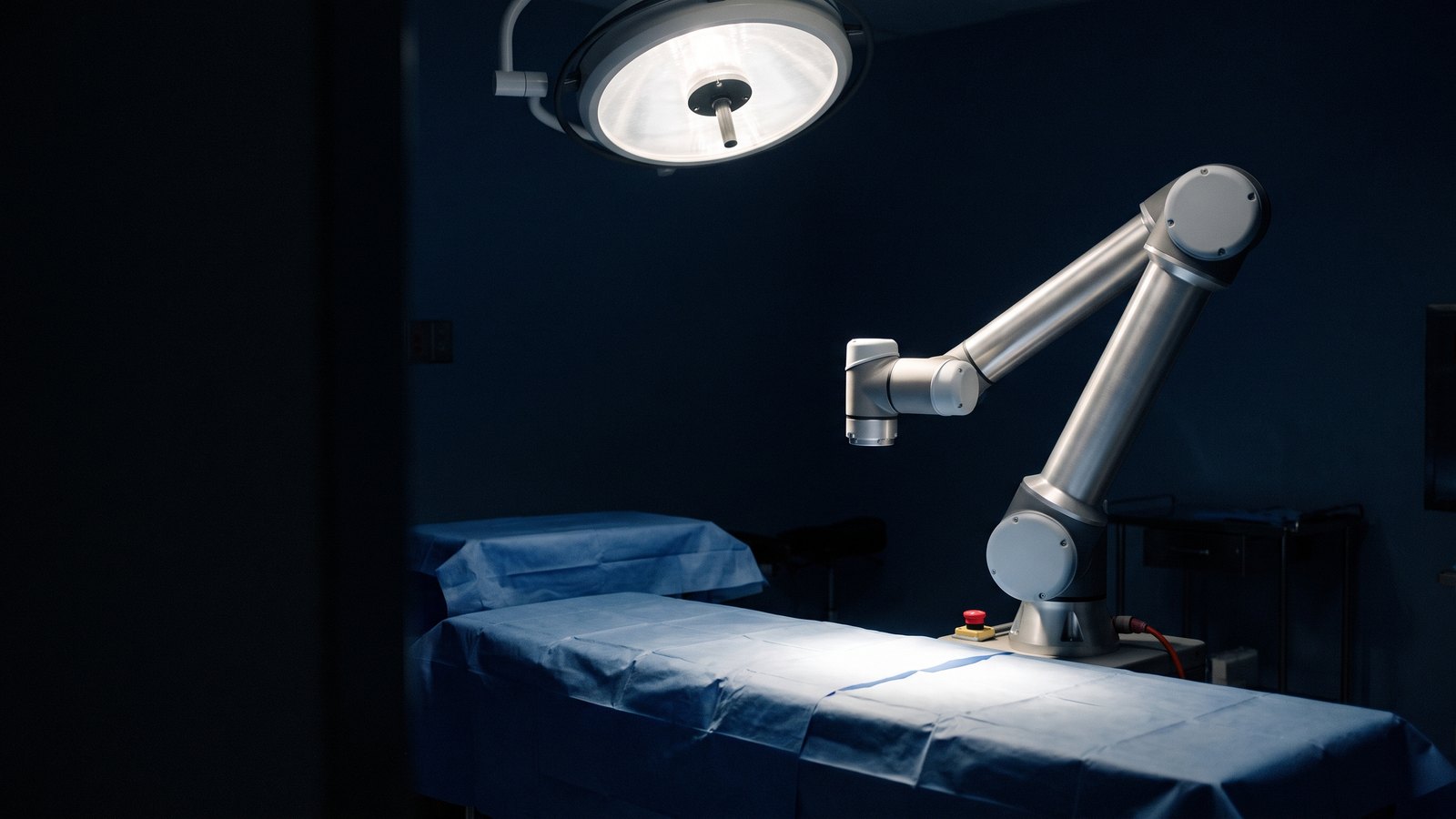 A surgical robotic arm, raised and idle, beside a draped operating table under one surgical light