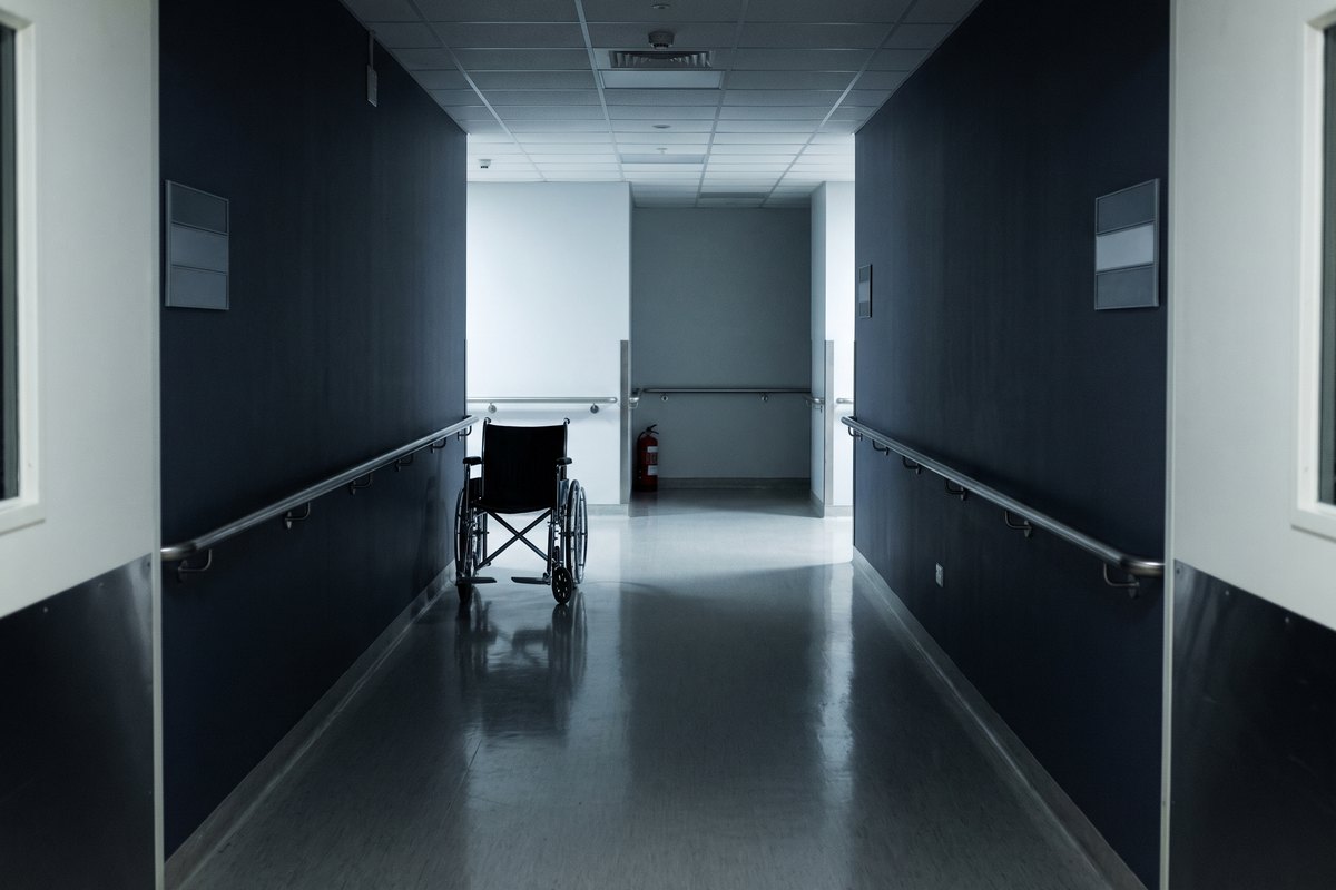 An empty wheelchair parked in a hospital corridor at night, with handrails along both walls